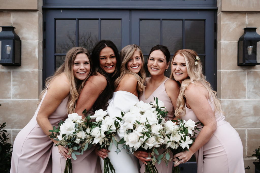 Bride and four bridesmaids in blush dresses cuddled together smiling at the camera in group photo