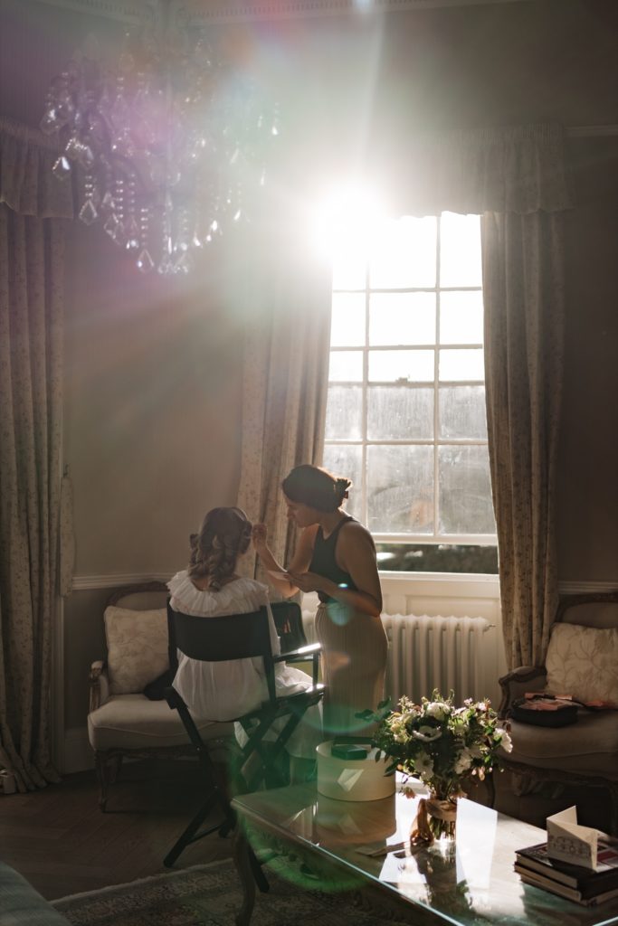 Bride having make up done sat in front of large window with light streaming through