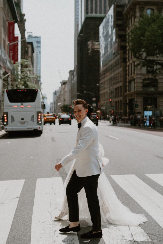 A couple in a white tux and a tulle Galia Lava wedding gown cross a New York City street