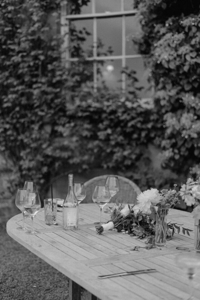 A black & white image of a table of discarded drinks & wedding flowers