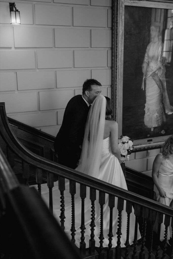 The father of the bride kisses the brides head as they walk down the stairs