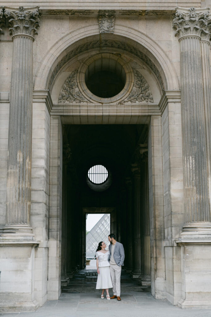 Chic couple stood under an arch outside the Louvre in Paris 