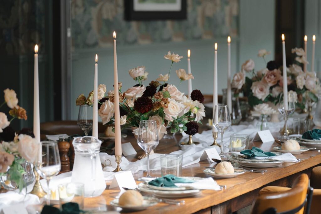 Wedding tablescape with lit taper candles in white and blush with flower urns filled with deep red and blush flowers